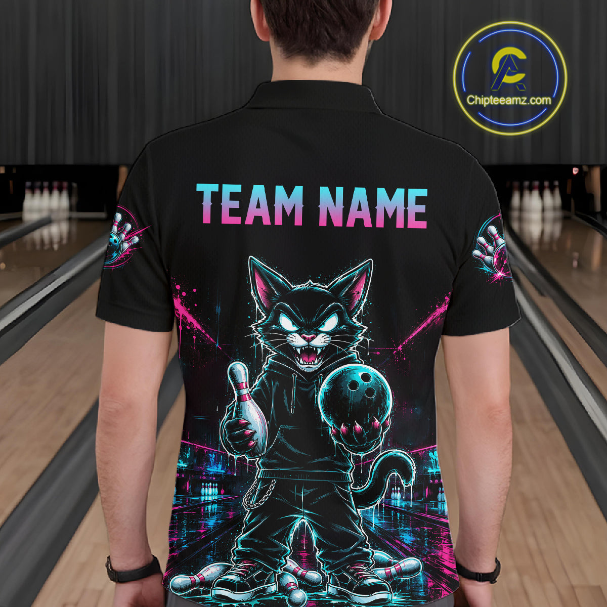 A person viewed from behind wearing a black short-sleeve bowling-themed shirt with a large neon cat graphic and the words 'TEAM NAME' across the upper back. The background shows bowling lanes, and a circular Chipteameinz.