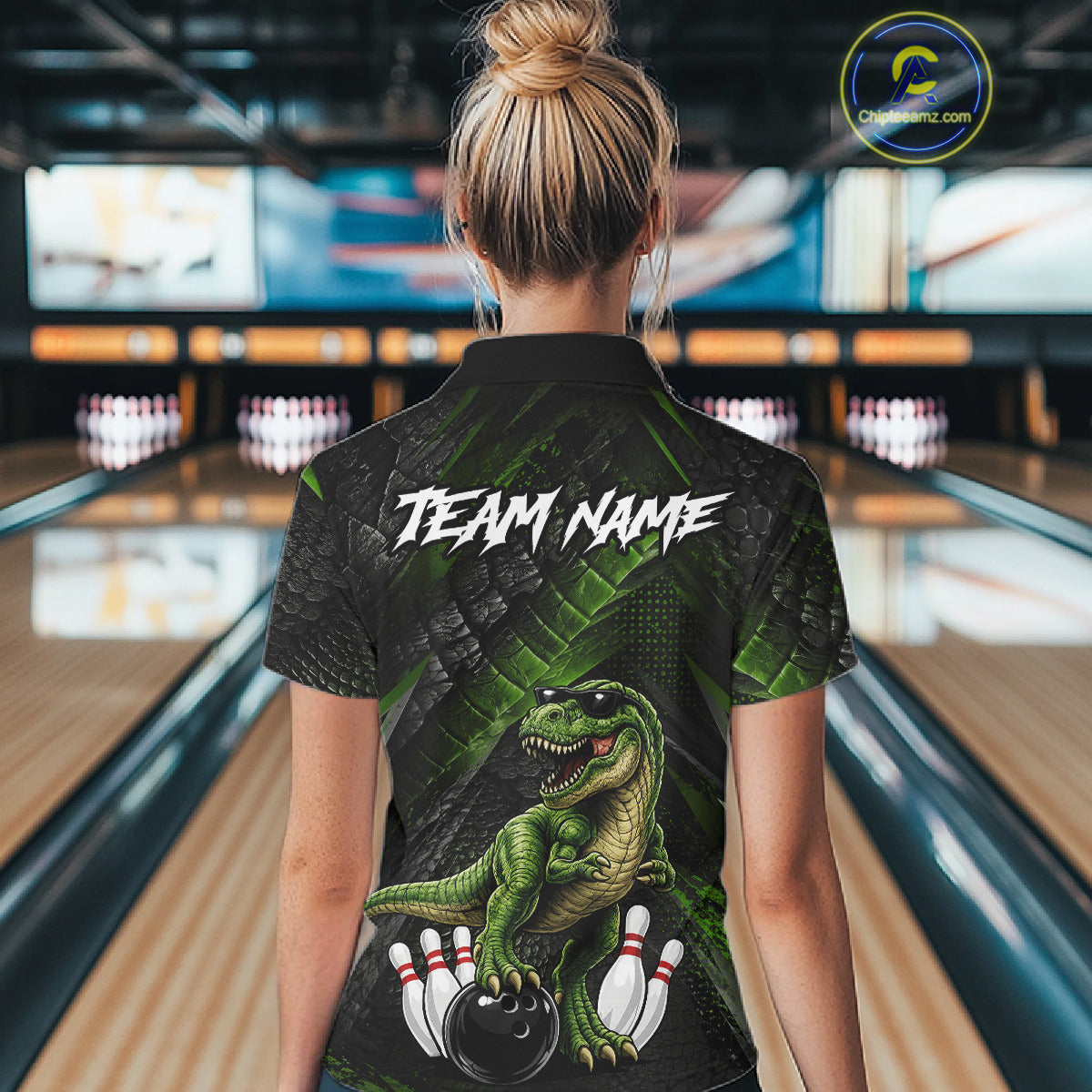 Women wearing bowling polo shirt featuring a dinosaur standing among bowling pins and ball artwork on black green textured background.