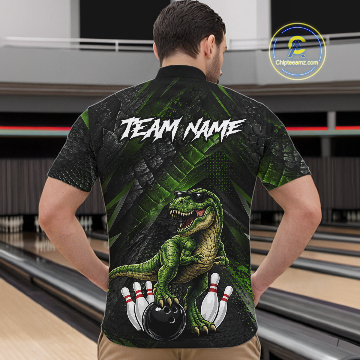 Man wearing bowling quarter zip shirt featuring a dinosaur standing among bowling pins and ball artwork on black green textured background.