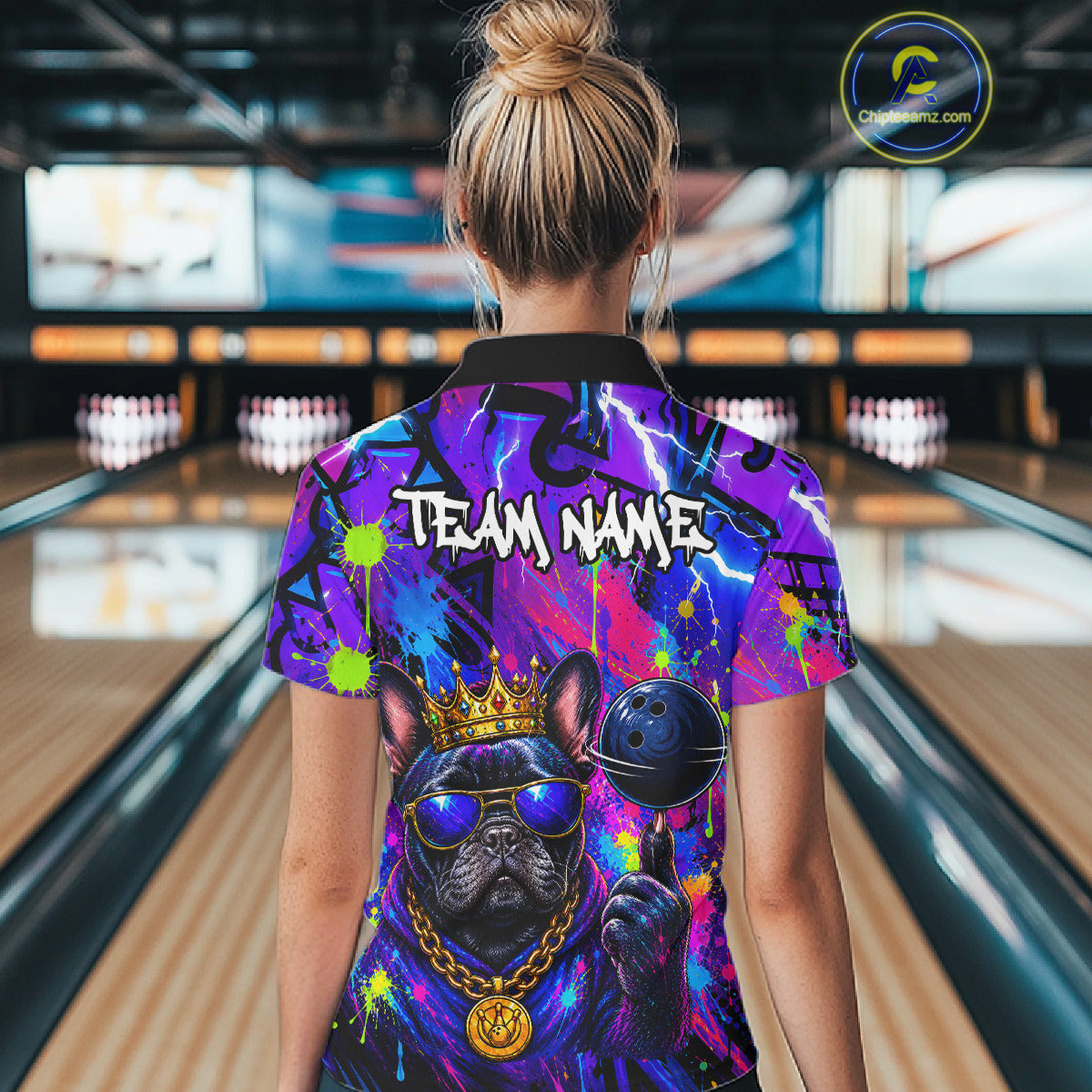 Women wearing personalized bowling polo shirt with a crowned bulldog holding a bowling ball, surrounded by paint effects and bold graphic patterns.