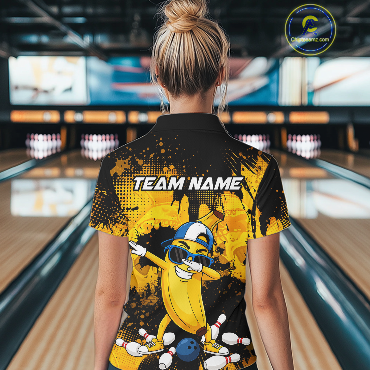 Woman wearing a black and yellow bowling polo featuring a cool banana mascot dabbing, bowling pins, a blue bowling ball, and custom team name text.
