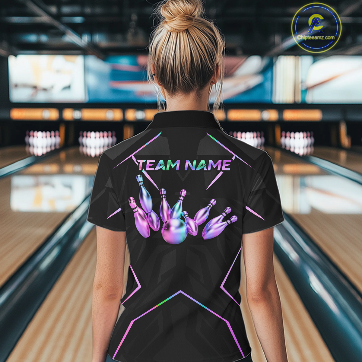 Person wearing a black bowling shirt with colorful design and 'TEAM NAME' text in a bowling alley.