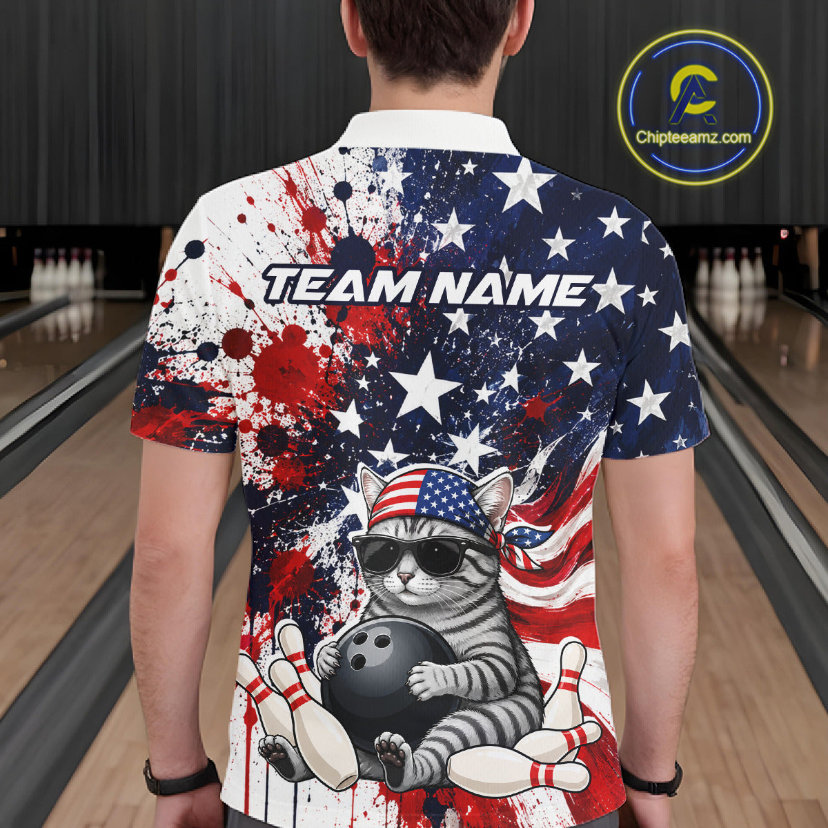 Person wearing a colorful bowling-themed shirt with a cat holding a bowling ball in a bowling alley.
