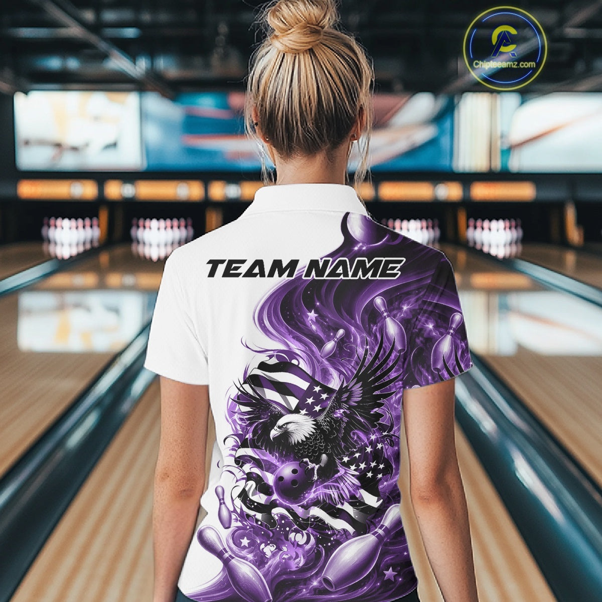 Female model back view in a bowling lane wearing a white and purple polo shirt with eagle artwork and flowing flag inspired graphics.