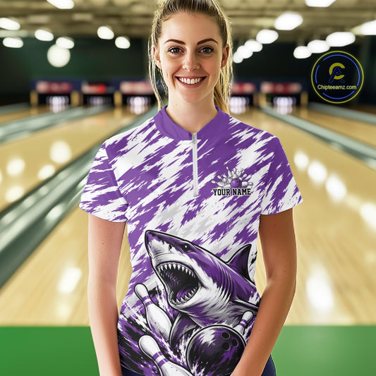 Person wearing a purple and white bowling shirt with a shark design in a bowling alley.