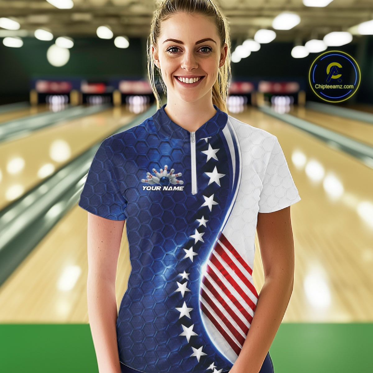 A woman stands in a bowling alley wearing a short-sleeve patriotic bowling shirt with a blue and white design, white stars, and red and white stripes. The shirt has a mock neck and a small logo on the left chest that reads 'YOUR NAME'.