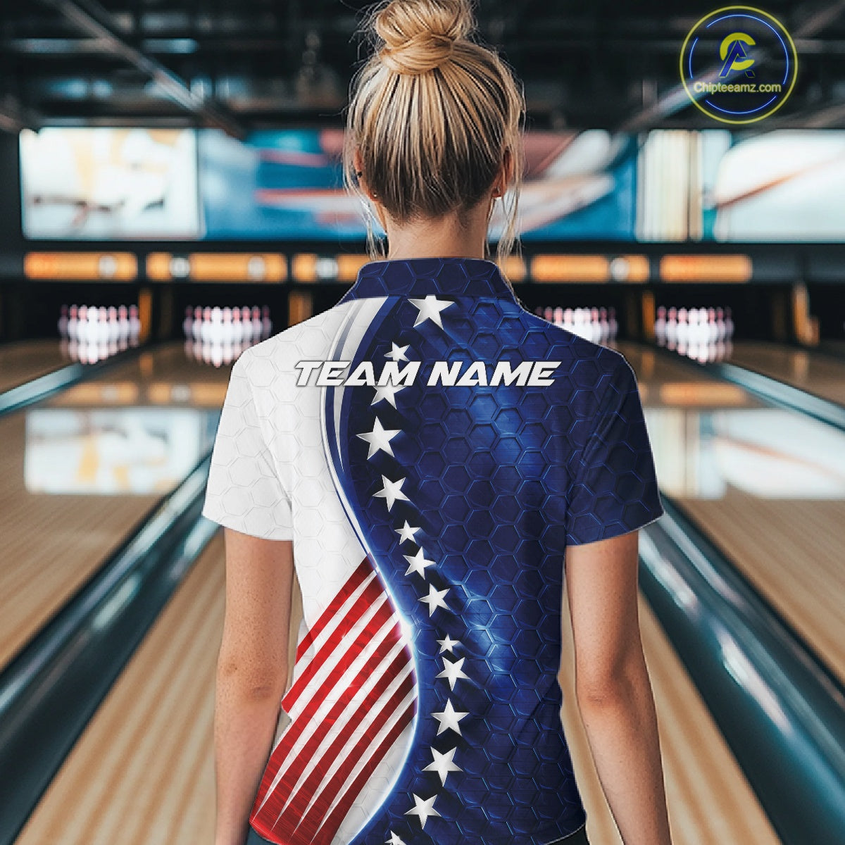 A woman viewed from behind wearing a short-sleeve bowling shirt with a US flag-inspired design, standing in a bowling alley. The shirt has a blue honeycomb pattern with white stars on one side and red and white stripes on the other, with 'TEAM NAME' printed across the upper back.