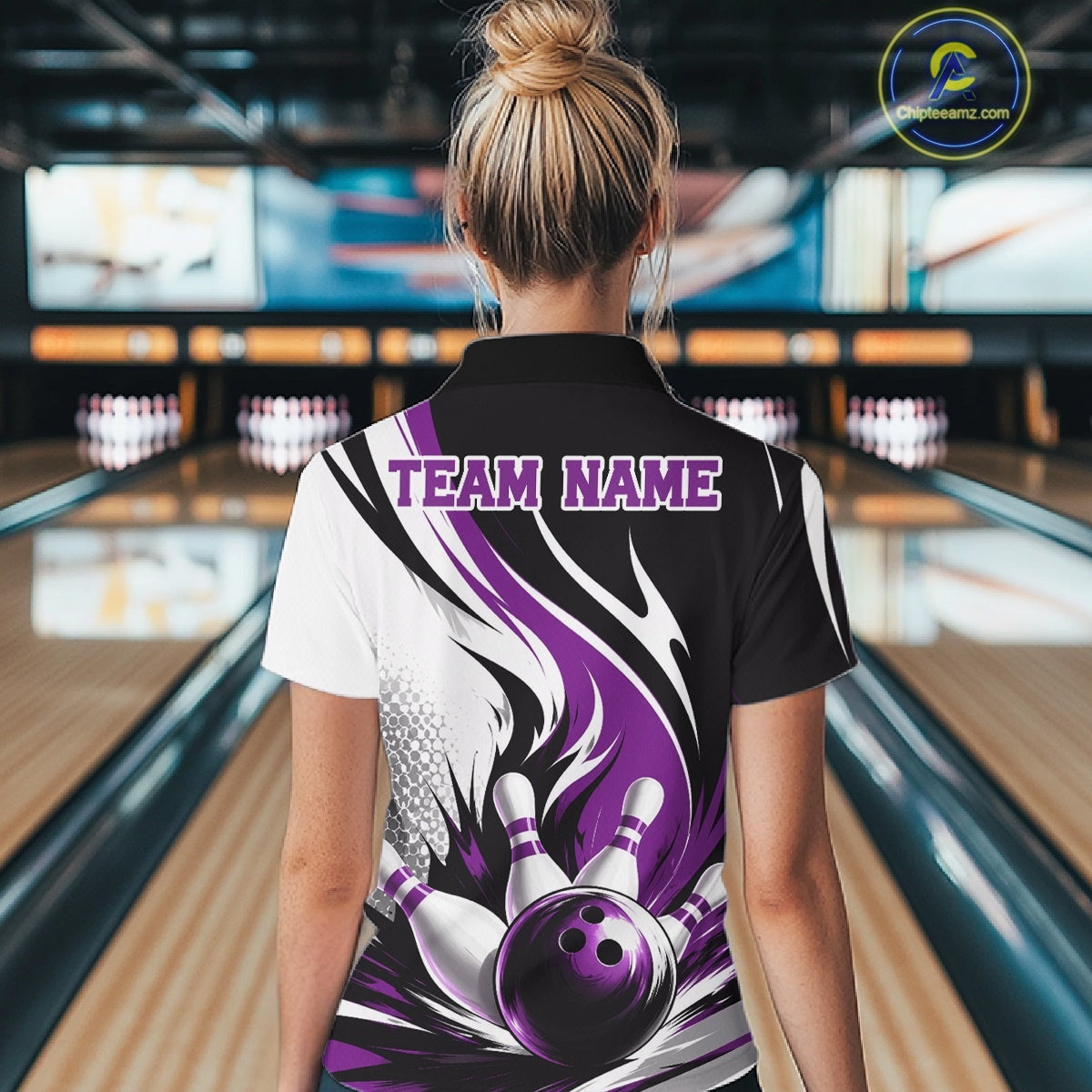 Back view of a female model wearing a white, black, and purple bowling polo shirt featuring a flaming bowling ball knocking down pins graphic at a bowling lane.
