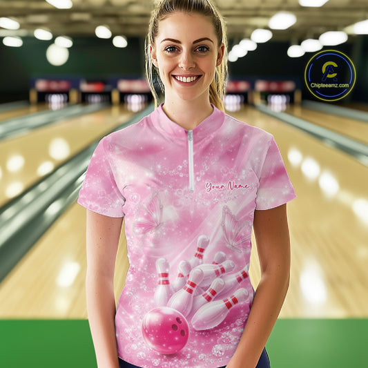 Female model in a bowling lane wearing a pink quarter zip shirt with butterfly and diamond sparkle bowling graphics.