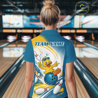 A woman viewed from behind wearing a blue bowling-themed short-sleeve polo shirt with a large graphic of a yellow duck bowling and the text 'TEAM NAME' on the back. The background shows a blurred bowling alley with lanes and pins.