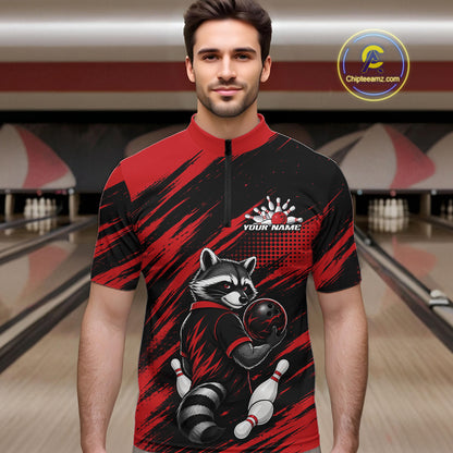 A man wearing a short-sleeve bowling-themed quarter-zip shirt with a raccoon graphic, set against a blurred bowling alley background. The shirt features a red and black brush-stroke pattern with a raccoon holding a bowling ball and pins.
