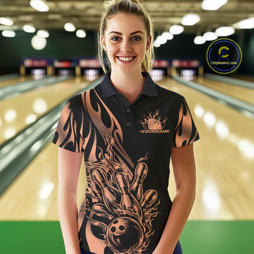 Female model front view at bowling lane wearing black polo shirt with rose gold tribal flame bowling ball hitting pins in dynamic sports action scene.