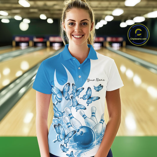 Female model wearing a white and blue bowling polo with butterfly artwork and bowling graphics, front view inside a bowling center