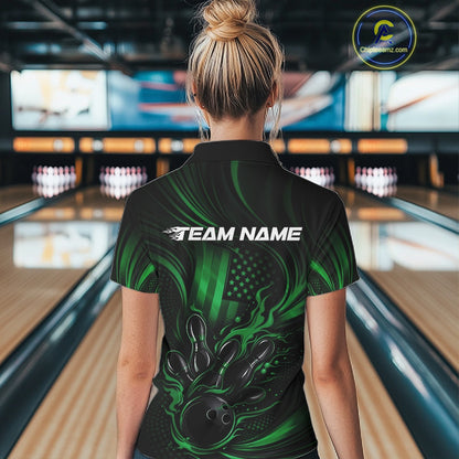 Back view of a female model in a bowling alley wearing a black and green quarter-zip shirt featuring a flaming bowling ball and patriotic pin design.