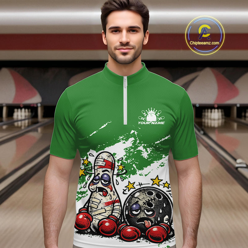 Male model at a bowling lane wearing a green and white quarter-zip shirt, humorous boxing bowling ball and pin artwork with playful energy.