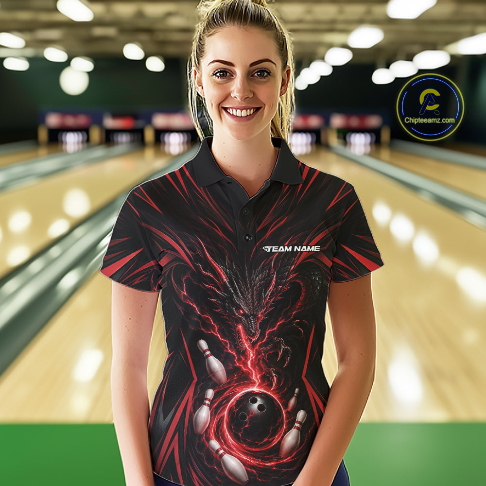 A woman stands in a bowling alley wearing a black short-sleeve polo shirt with a red and black dragon bowling-themed graphic print and the text 'YOUR NAME' on the chest.