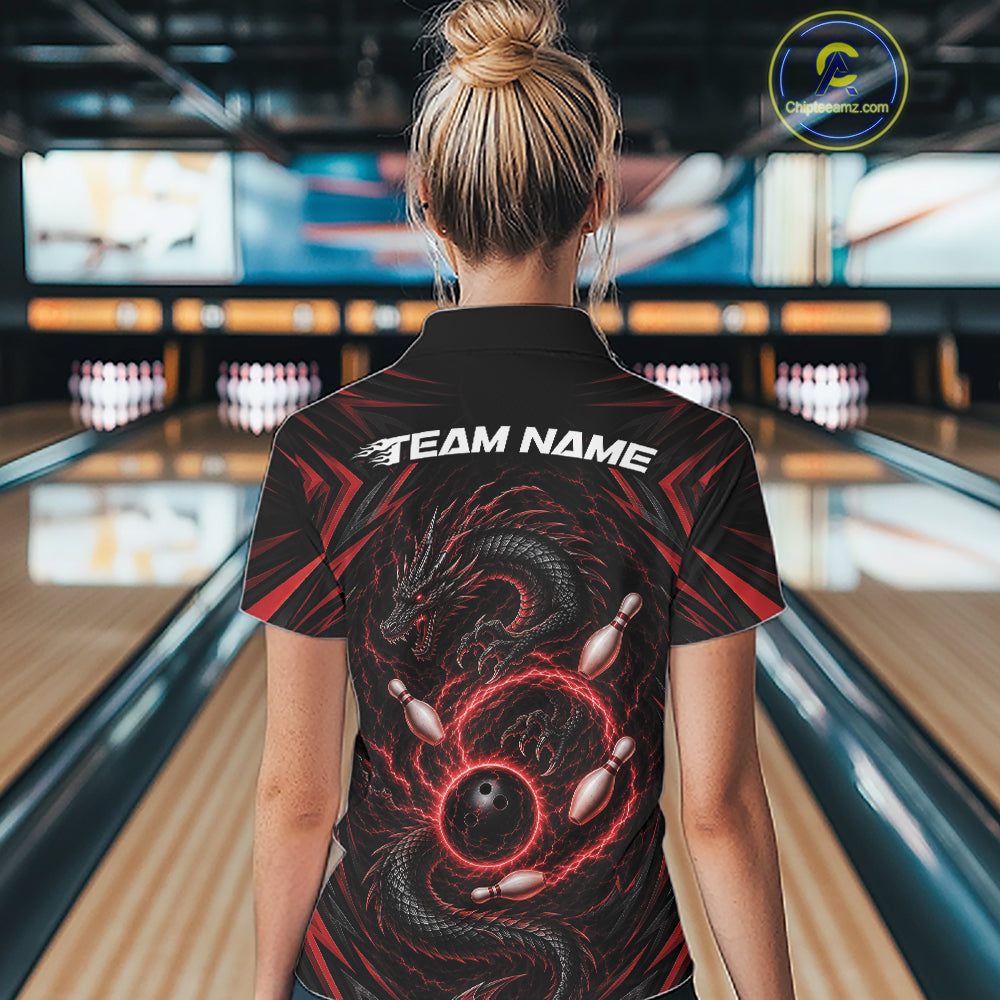 A woman viewed from behind wearing a black bowling short-sleeve polo shirt with a red and black dragon graphic and white 'TEAM NAME' text on the back, standing in a bowling alley.