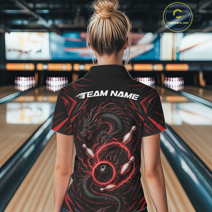 A woman viewed from behind wearing a black bowling short-sleeve polo shirt with a red and black dragon graphic and white 'TEAM NAME' text on the back, standing in a bowling alley.