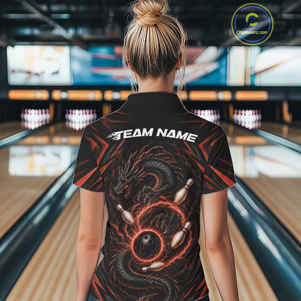 A woman viewed from behind wearing a black bowling-themed short-sleeve quarter zip shirt with a orange and black dragon graphic and white 'TEAM NAME' text on the back, standing in a bowling alley.
