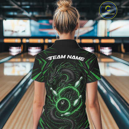 A woman viewed from behind wearing a black bowling-themed short-sleeve polo shirt with a green dragon and bowling ball graphic, and the text 'TEAM NAME' across the shoulders. The background shows a blurred bowling alley with lanes and pins.