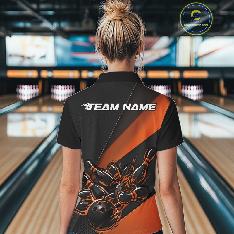 Back view female model inside bowling alley wearing black and orange quarter zip shirt with flame bowling action graphics