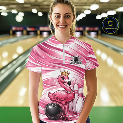Female model at a bowling lane wearing a pink bowling quarter-zip shirt with a crowned flamingo, bowling ball, and bowling pin graphics.