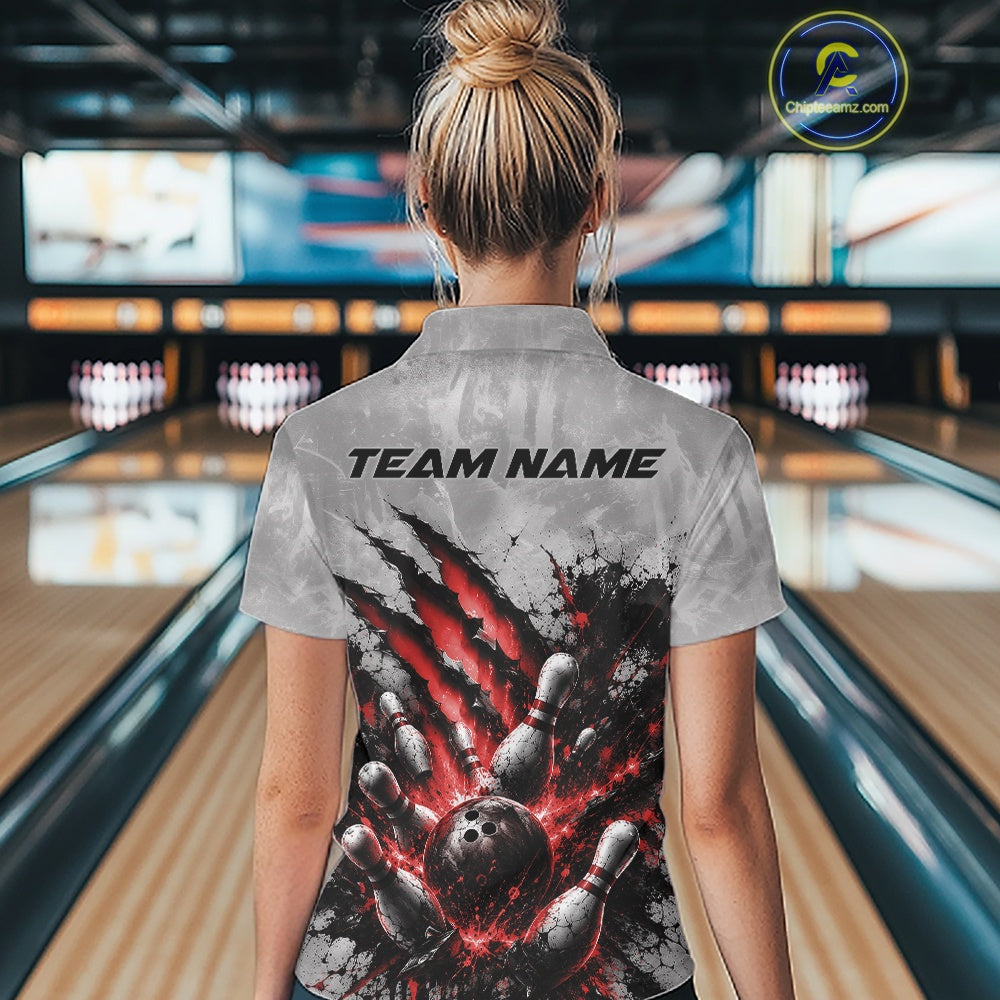 Back view of a female model wearing a gray bowling polo shirt featuring a dramatic red bowling ball and pins graphic with claw-mark artwork in a bowling lane.