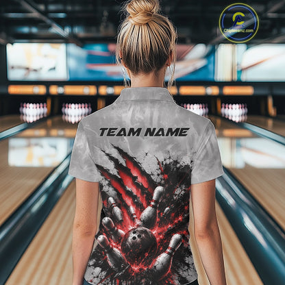Back view of a female model wearing a gray bowling polo shirt featuring a dramatic red bowling ball and pins graphic with claw-mark artwork in a bowling lane.