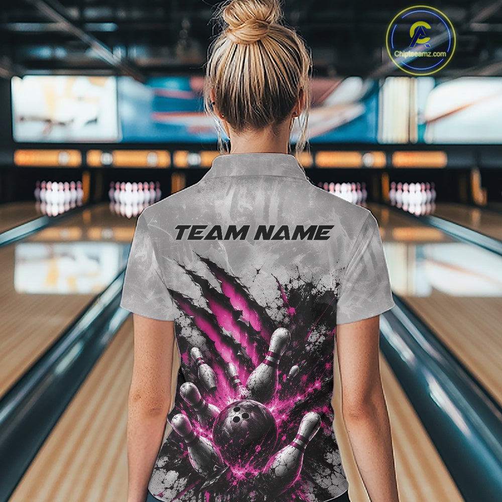 Back view of a female model wearing a gray bowling polo shirt showcasing a dramatic pink bowling ball and pins graphic with claw-mark artwork at a bowling lane.