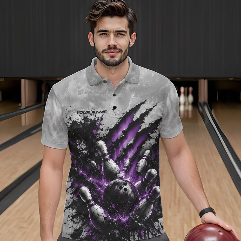 Male model shown from the front wearing a gray bowling polo shirt featuring a dramatic purple bowling ball striking pins graphic with claw-mark artwork at a bowling lane.