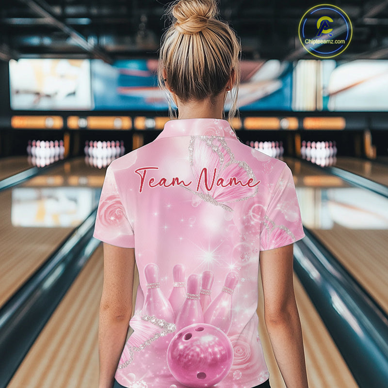 Back view of a female model in a bowling lane wearing a quarter-zip bowling shirt featuring pink glitter butterflies, bowling pins, and bowling ball artwork.