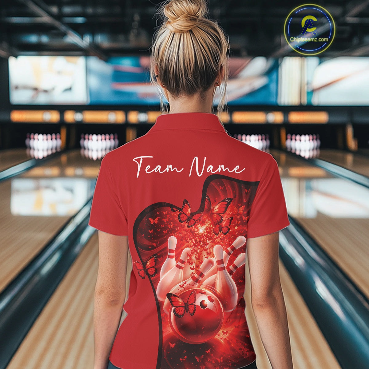 Back view of a women s red bowling polo shirt displaying butterfly artwork and bowling graphics inside a bowling center.