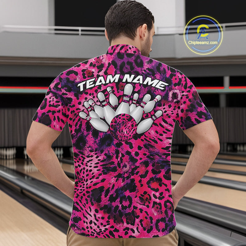 Back view of a man standing at a bowling alley, wearing a pink, purple, and black leopard-print bowling polo with “Team Name” and bowling pins on the back.
