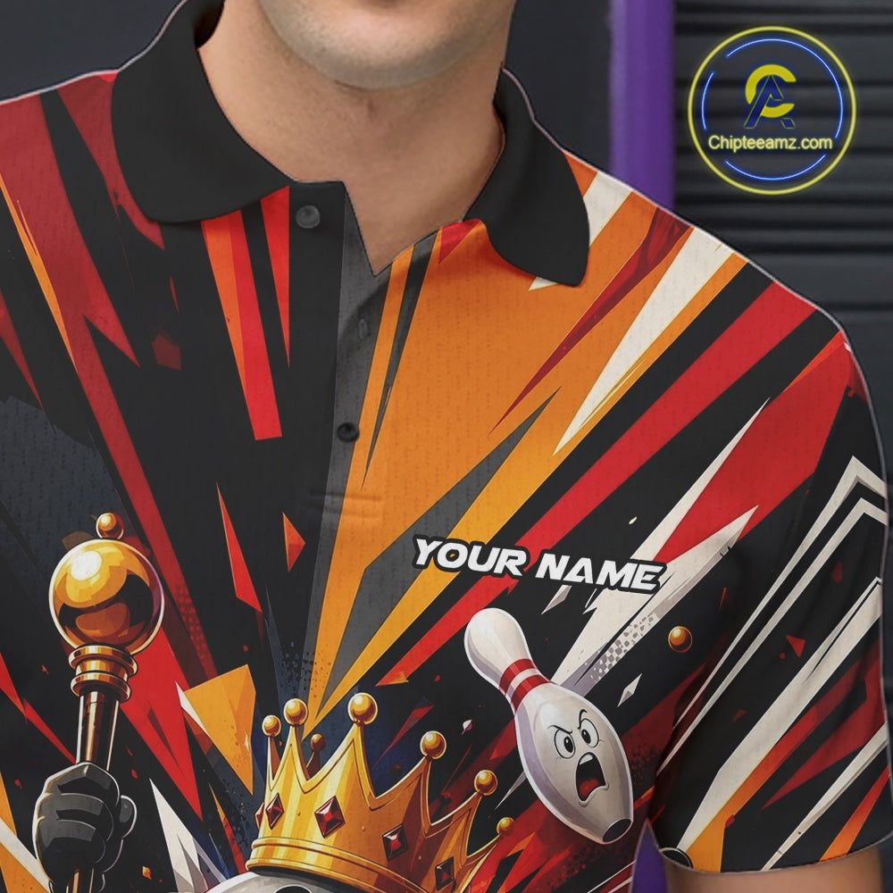Close-up of the left chest on a black, red, and orange bowling polo shirt featuring a crowned cartoon bowling ball holding a royal scepter with animated bowling pins and colorful burst artwork.