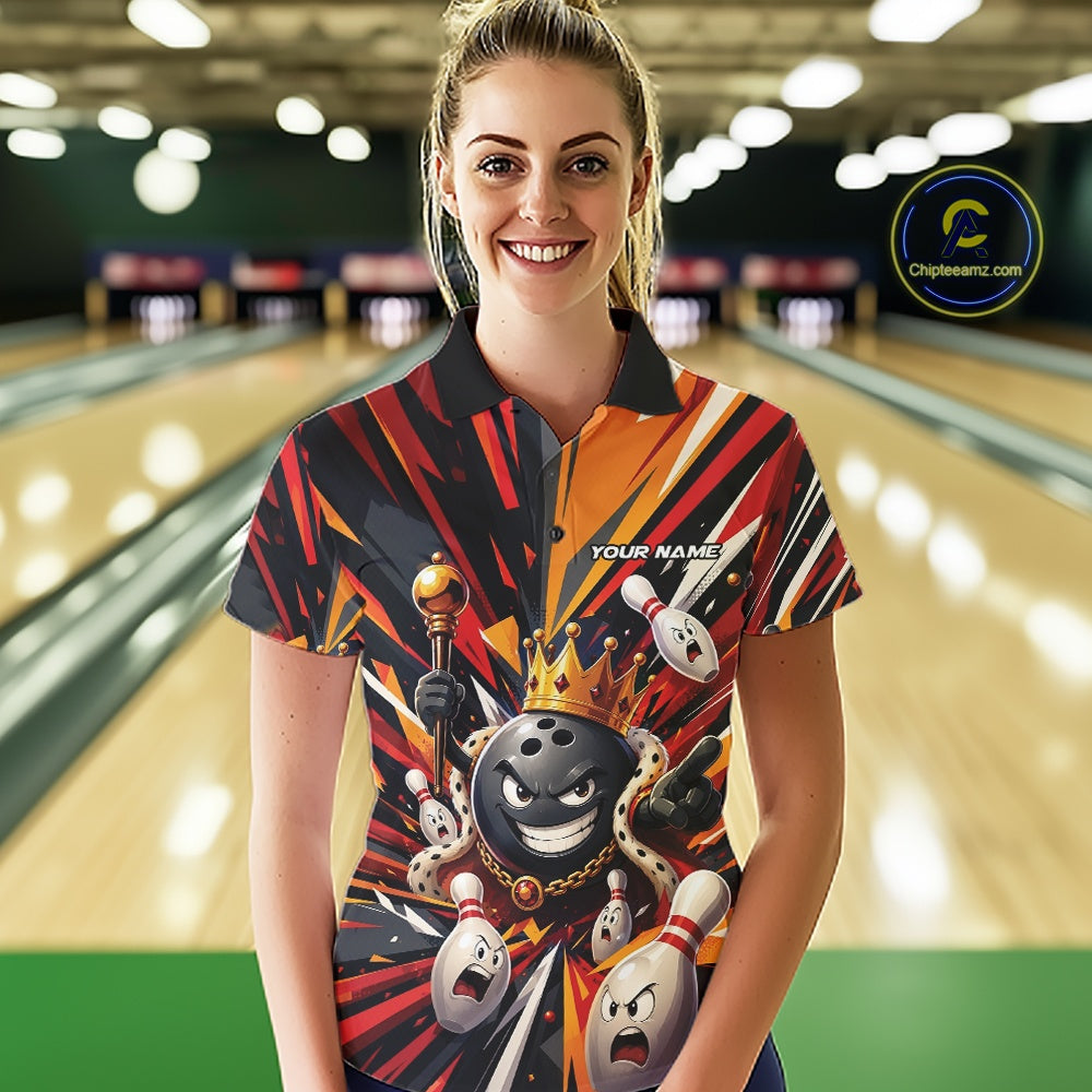 Front view of a female model wearing a black, red, and orange bowling polo shirt featuring a crowned cartoon bowling ball with a royal scepter leading animated bowling pins through vibrant bursts of color in a bowling lane.