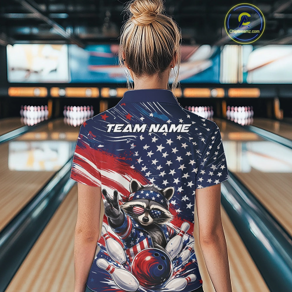 Back view of a female model at a bowling lane wearing a bowling polo shirt with a patriotic raccoon flashing a peace sign as a red, white, and blue bowling ball crashes through falling pins against a flowing American flag backdrop.