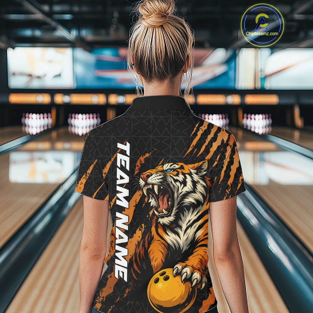 Back view of a female model in a bowling lane wearing a black and yellow bowling polo shirt featuring a roaring tiger holding a yellow bowling ball with orange claw-stripe graphics and a geometric background pattern.