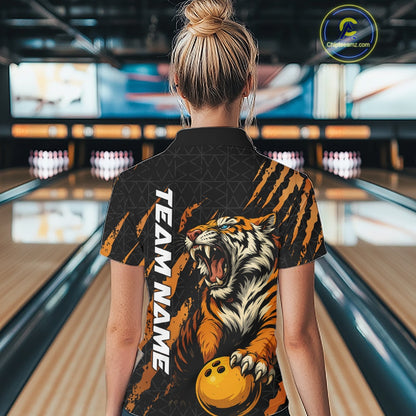 Back view of a female model in a bowling lane wearing a black and yellow bowling polo shirt featuring a roaring tiger holding a yellow bowling ball with orange claw-stripe graphics and a geometric background pattern.