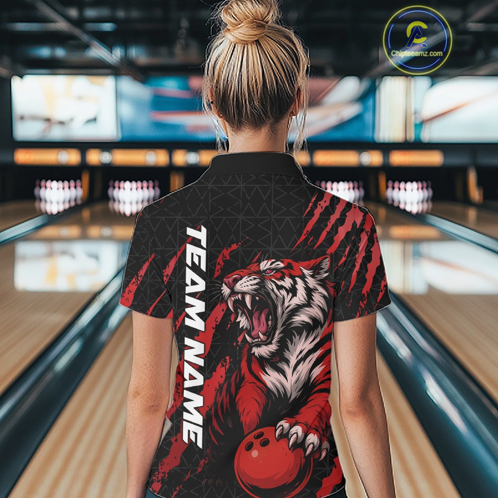 Back view of a female model wearing a black and red bowling polo shirt in a bowling lane, featuring a roaring tiger holding a red bowling ball with matching red claw-stripe artwork and a geometric background pattern.