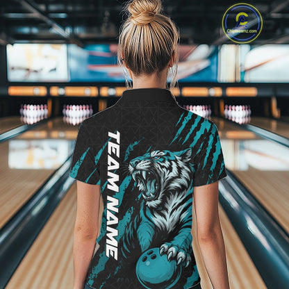 Back view of a female model in a bowling lane wearing a black and teal blue bowling polo shirt featuring a roaring tiger holding a teal blue bowling ball with teal blue claw-stripe artwork and a geometric background pattern.