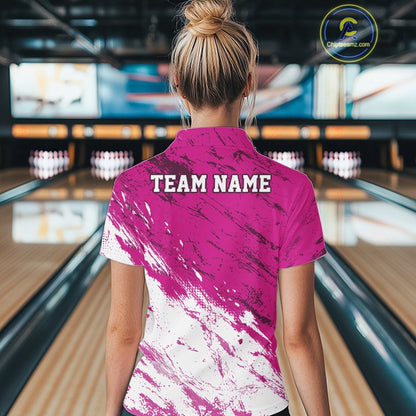 Person wearing a pink and white bowling shirt with 'TEAM NAME' on the back in a bowling alley.