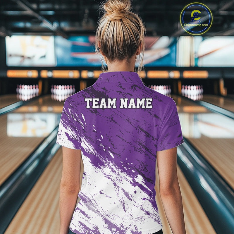 Back view of a female model in a bowling alley wearing a bowling polo shirt featuring a white and purple paint splatter distressed sportswear design.
