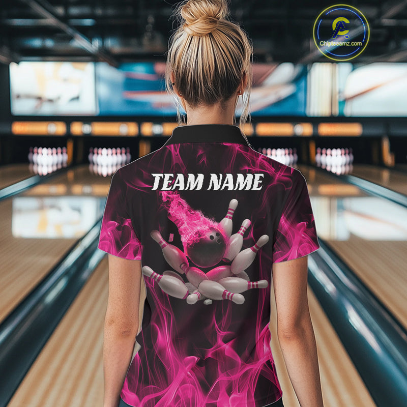 Back view of a female model in a bowling lane wearing a black and pink polo shirt featuring a bowling ball crashing into scattered pins with a flames background.