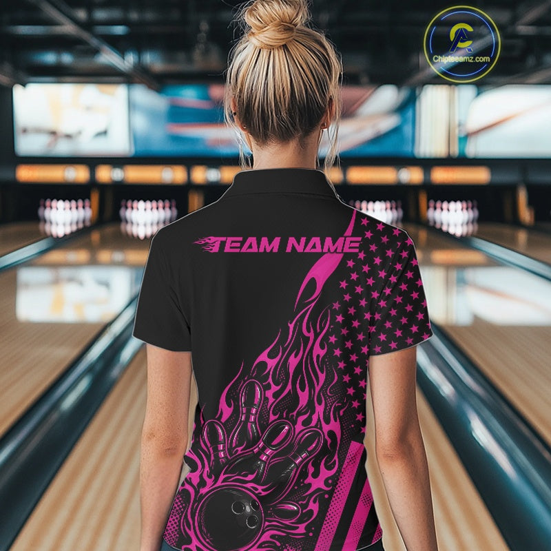 Back view of a female model in a bowling alley wearing a black polo shirt showcasing a pink flaming bowling ball hitting the pins.