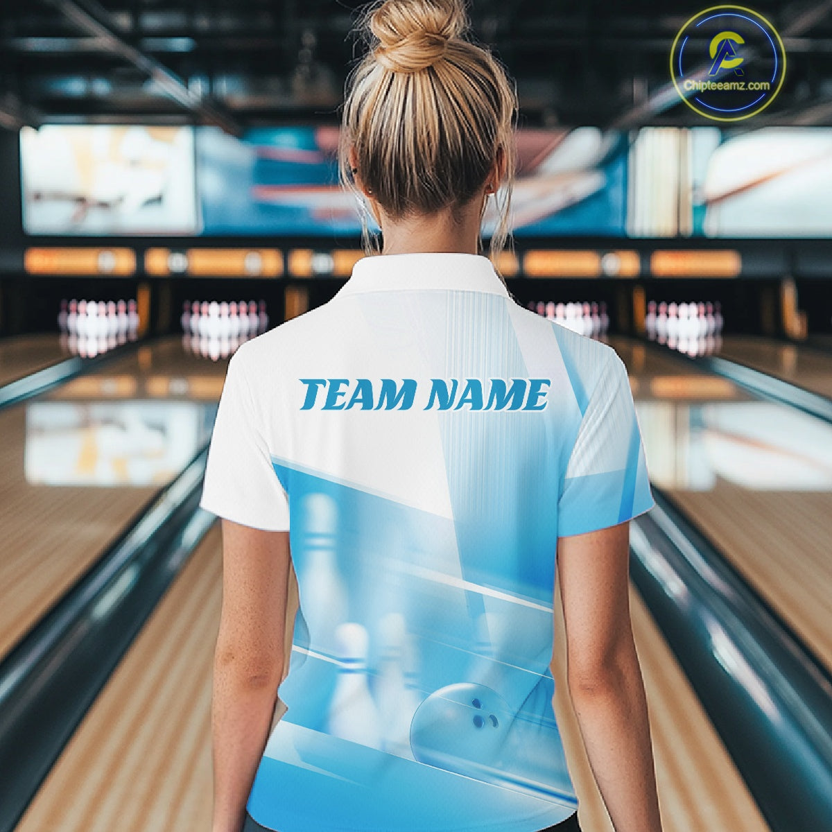 Back view of a female model in a bowling lane wearing a white and blue polo shirt with bowling ball and pins in a pink geometric pattern.
