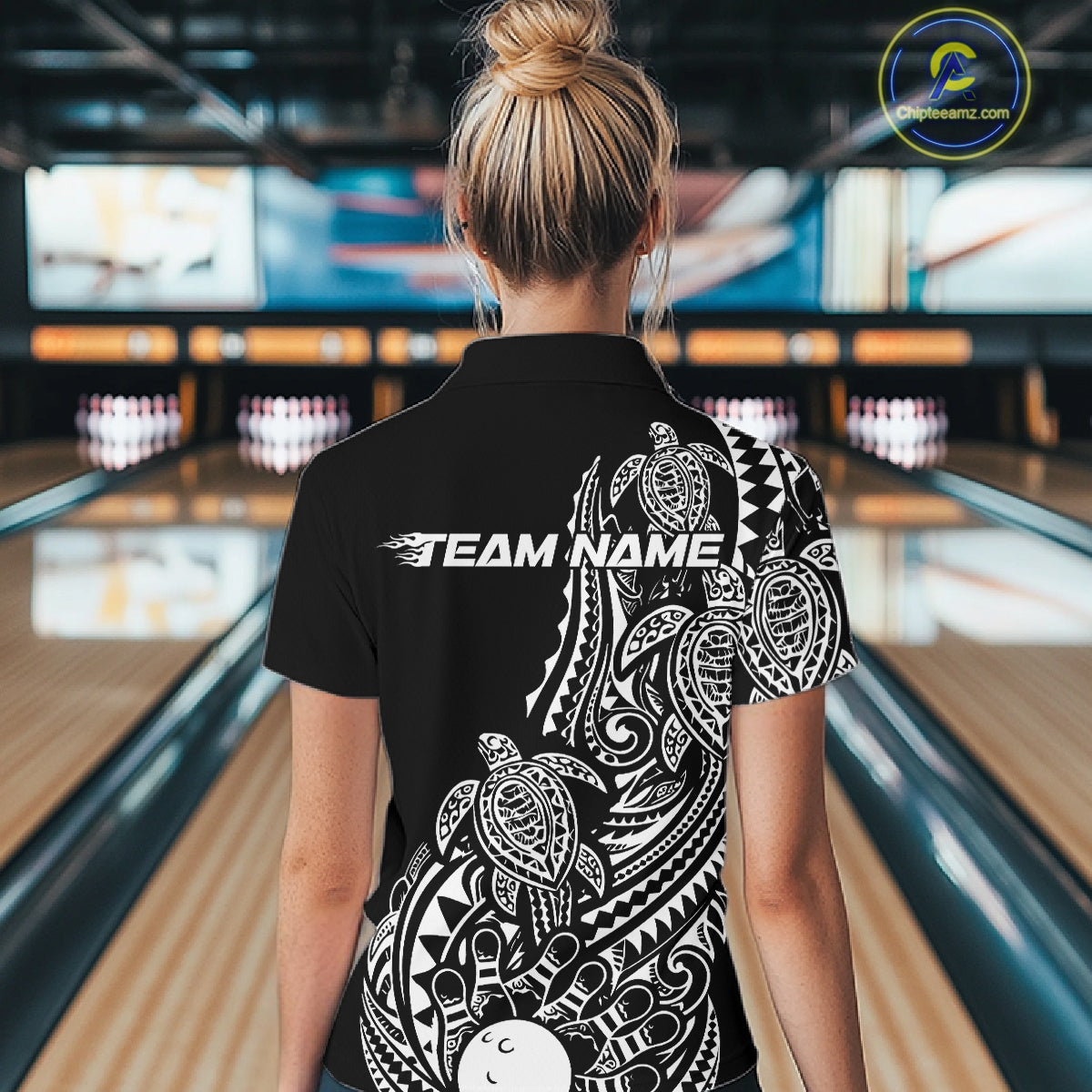 Back view of a female model in a black and white bowling polo shirt featuring bowling ball and pin artwork surrounded by tribal swirls and turtle Polynesian patterns.