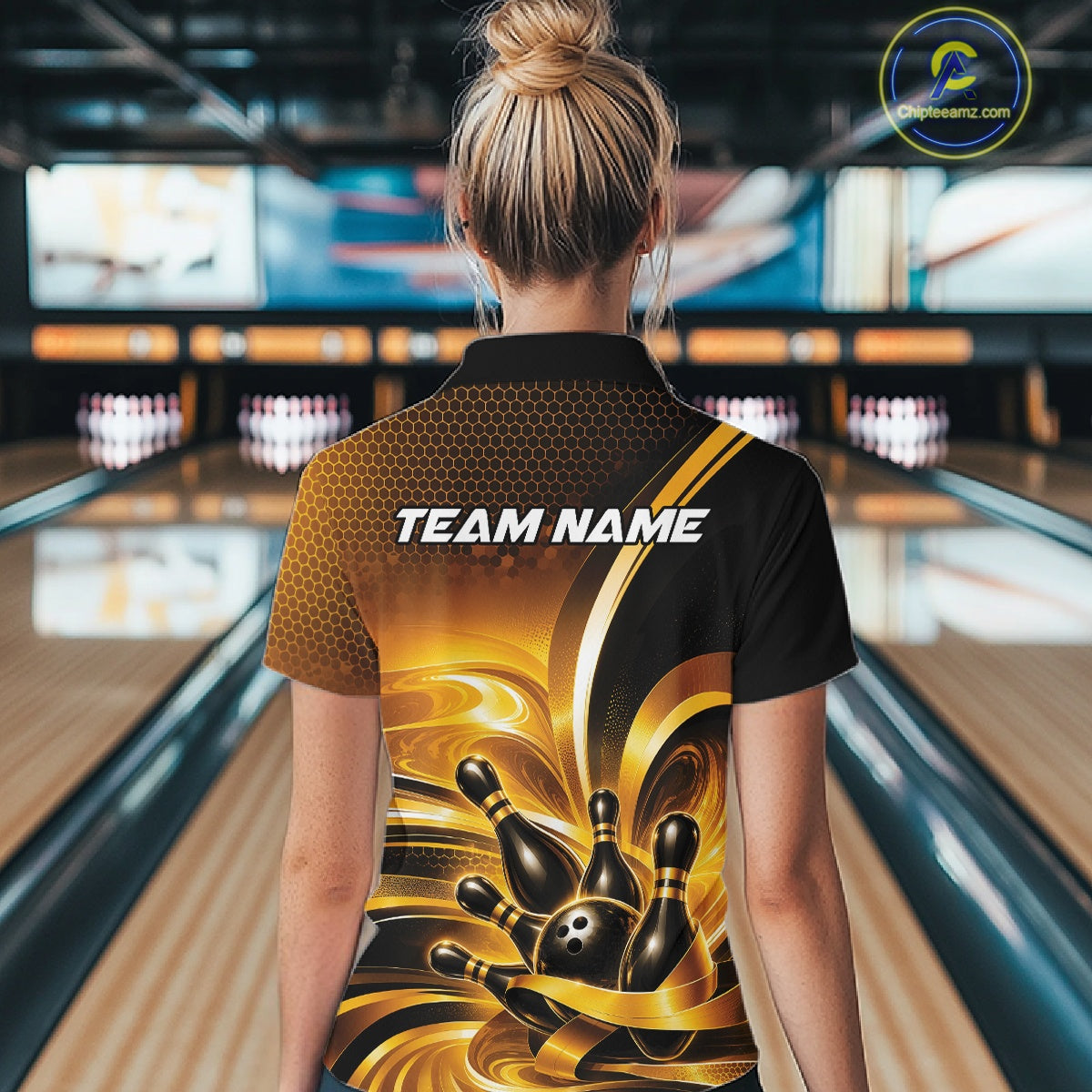 Back view of a female model at a bowling lane wearing a bowling polo shirt with glossy gold and black bowling ball and pins artwork.