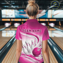 Load image into Gallery viewer, Back view of a female model wearing a white and pink bowling quarter-zip shirt in a bowling alley featuring flowing abstract wave patterns and a glossy bowling ball striking a set of pins