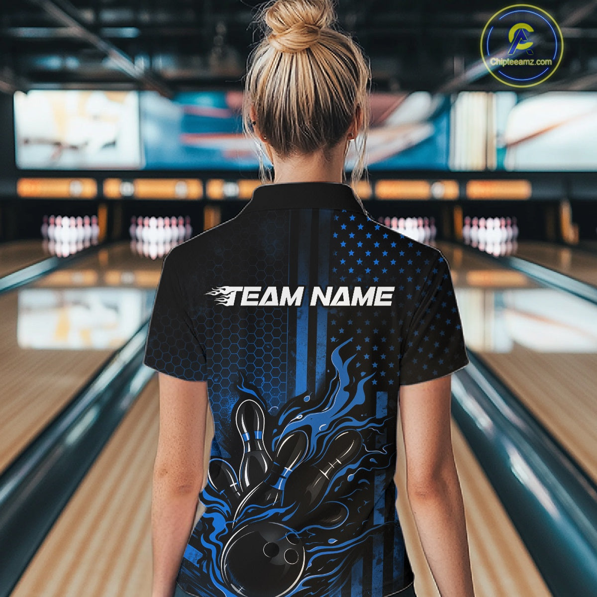 Back view of a female model in a bowling alley wearing a black and blue quarter-zip shirt showcasing a bowling strike motif with flame effects.
