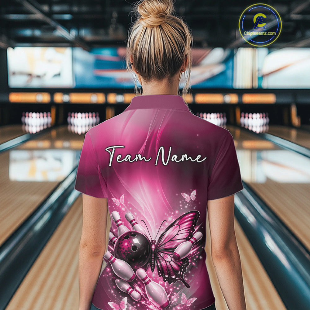 Back view of a female model at a bowling lane wearing a pink bowling quarter-zip shirt with a butterfly beside a bowling ball and scattered pins.